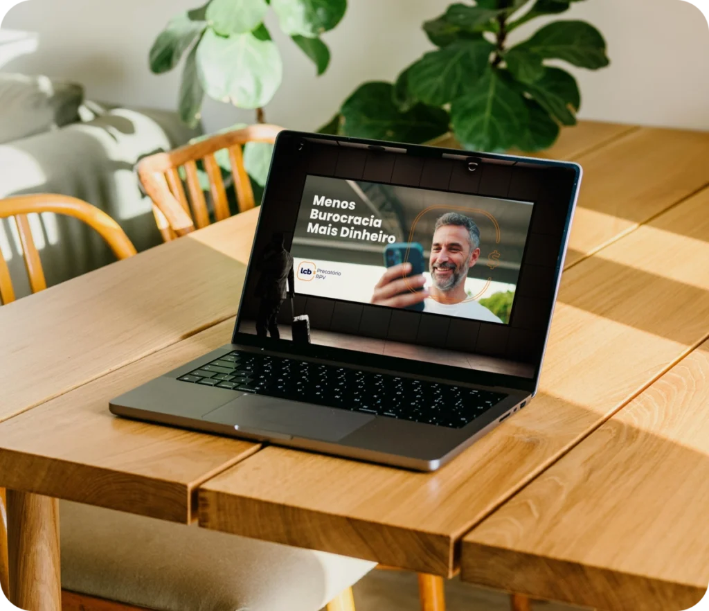 Laptop exibindo vídeo com o texto "Menos Burocracia Mais Dinheiro" e um homem sorrindo.