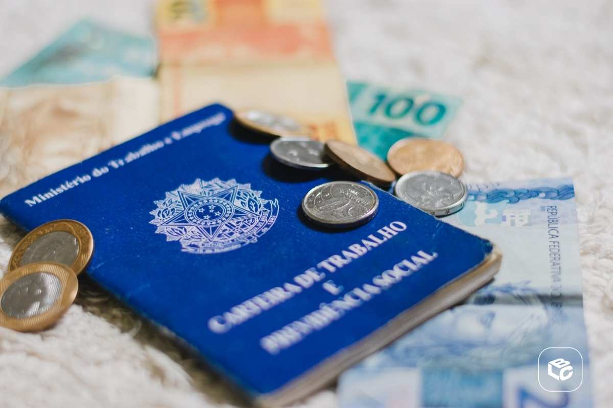 Carteira de Trabalho e Previdência Social com dinheiro e moedas brasileiras