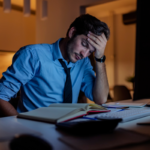 Homem de camisa azul estressado em frente a um computador à noite